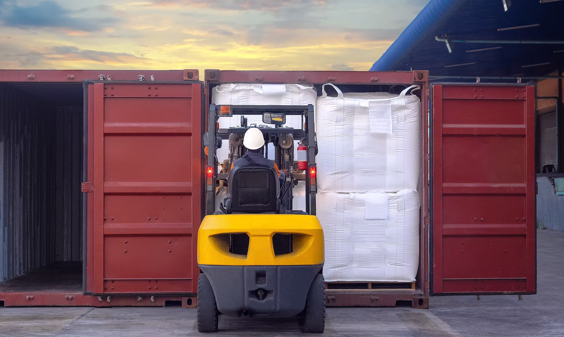 Forklift loading palletised bags into a shipping container at sunset